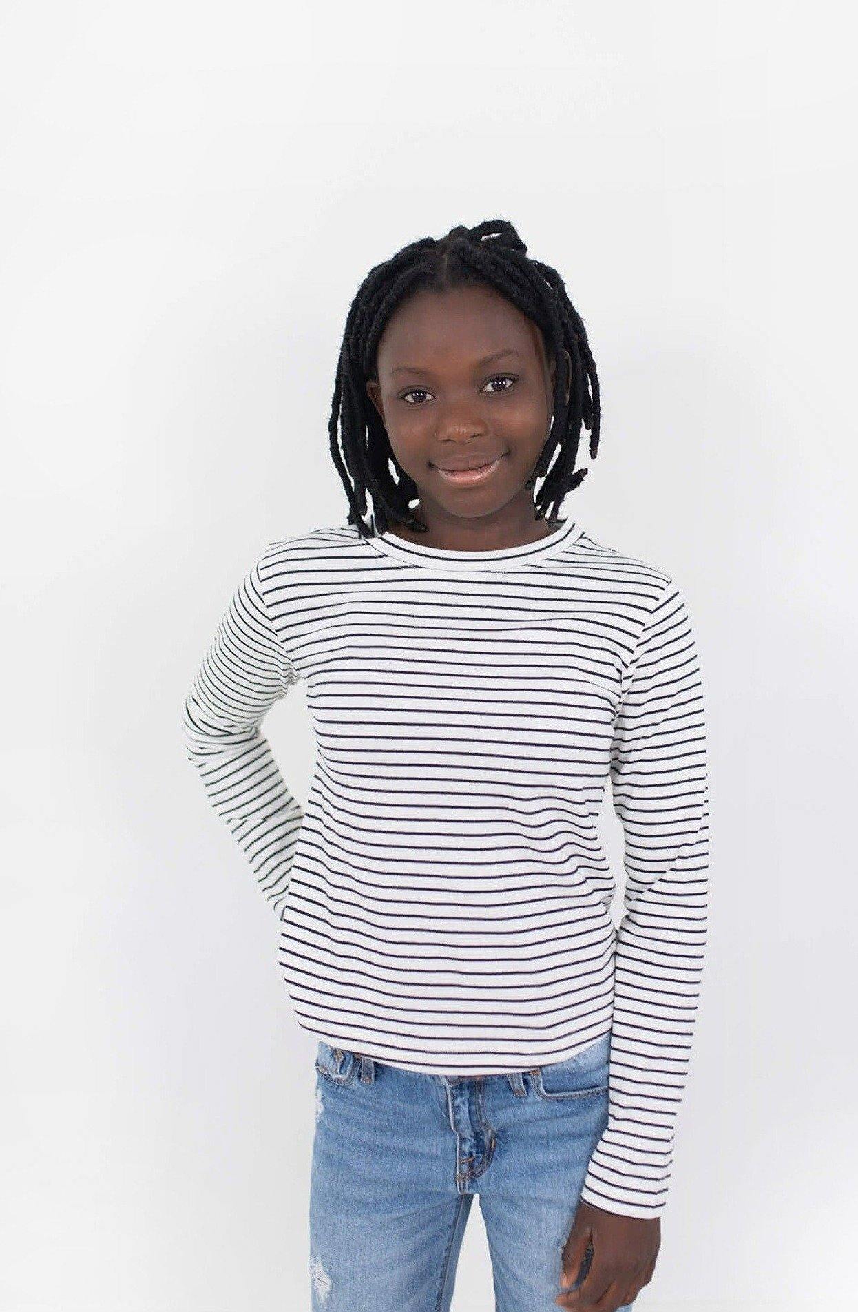 Girl wearing white organic cotton long sleeve shirt with black stripes.