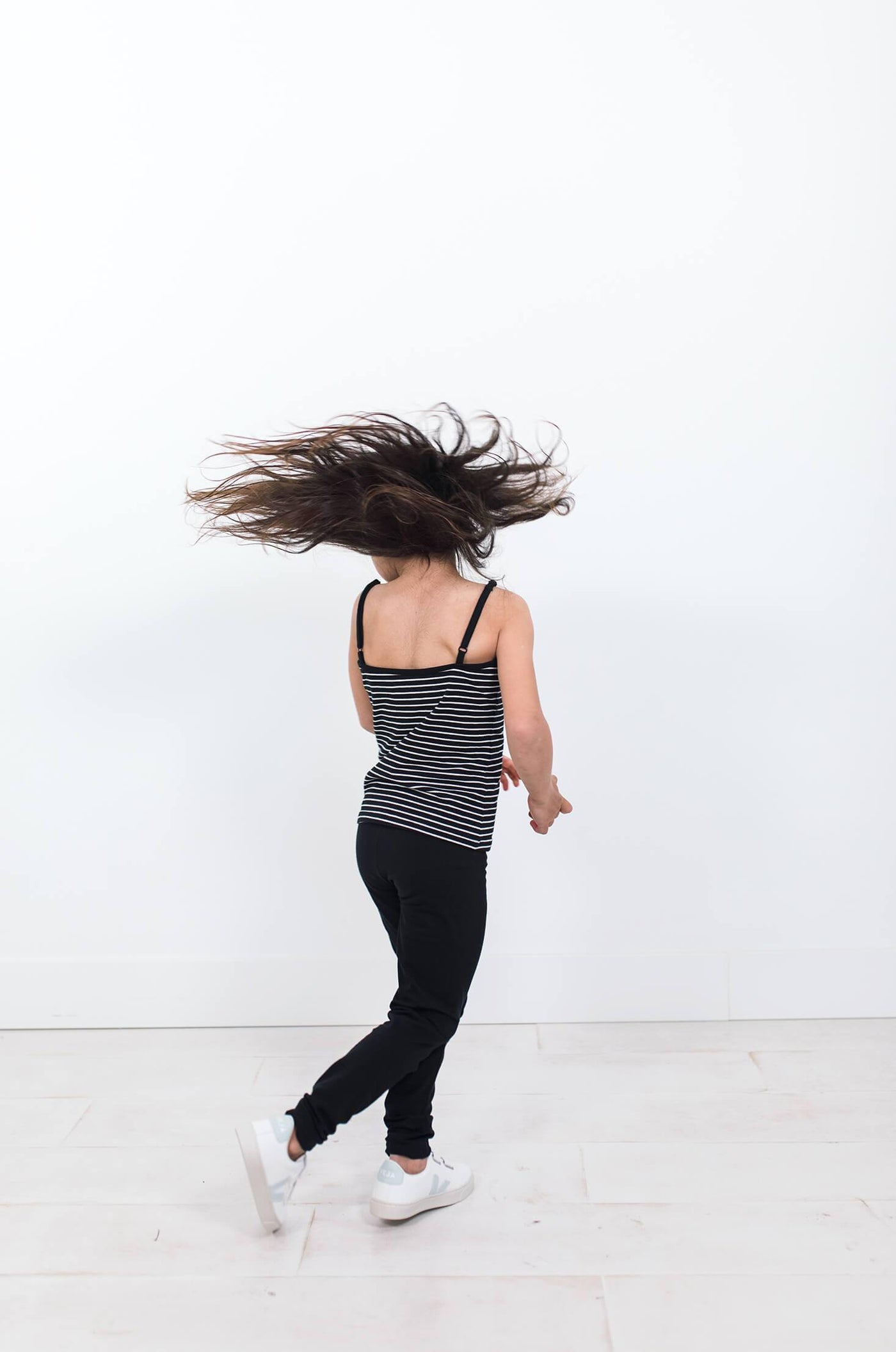 Girl spinning with long hair wearing black organic cotton cami with white stripes.